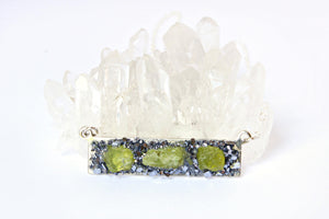Peridot crystal jewelry necklace atop a white crystal background